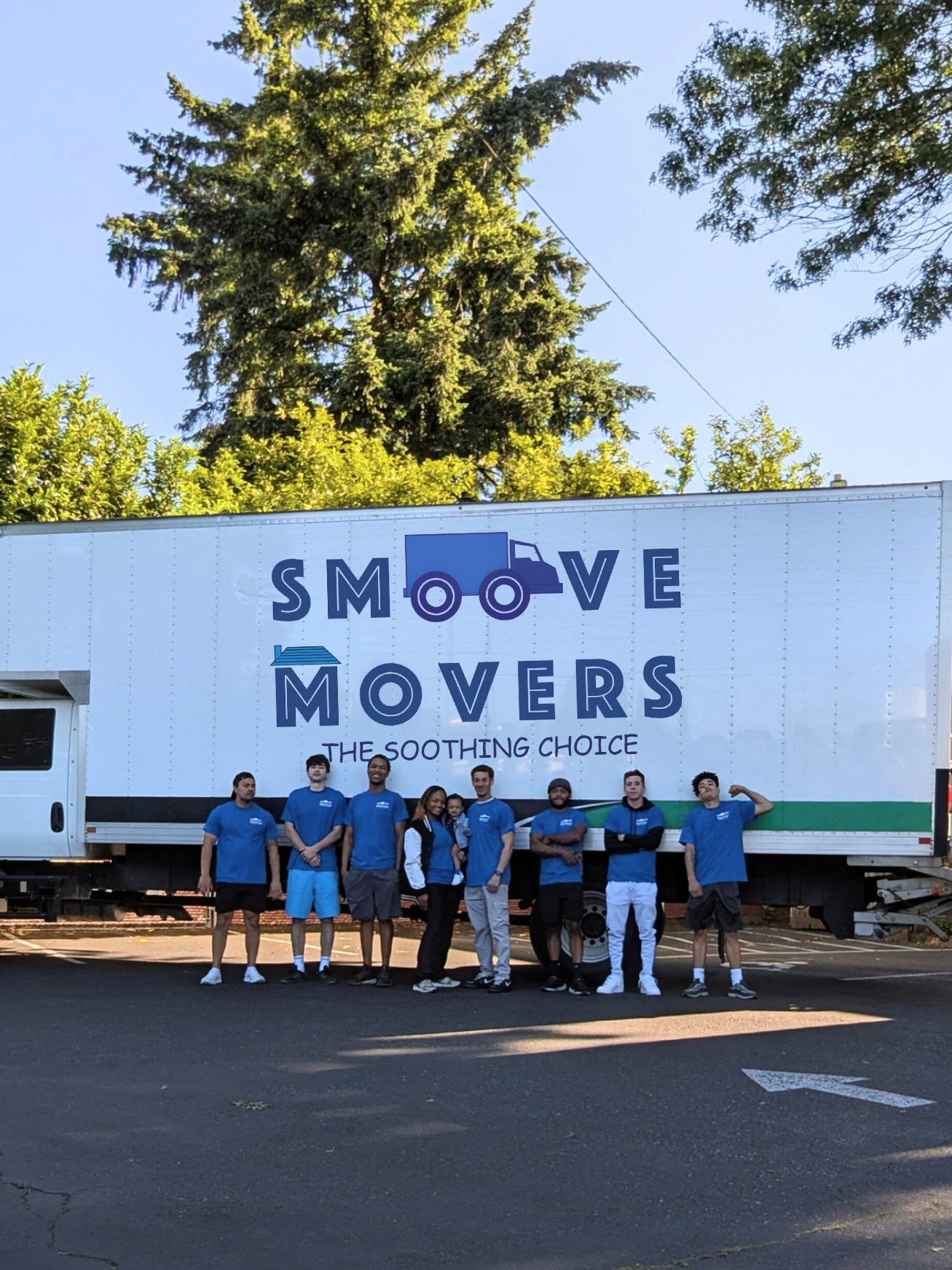 Group of movers in blue shirts standing in front of a large white moving truck with 'MOVERS' lettering and a blue truck logo, outdoors on a sunny day